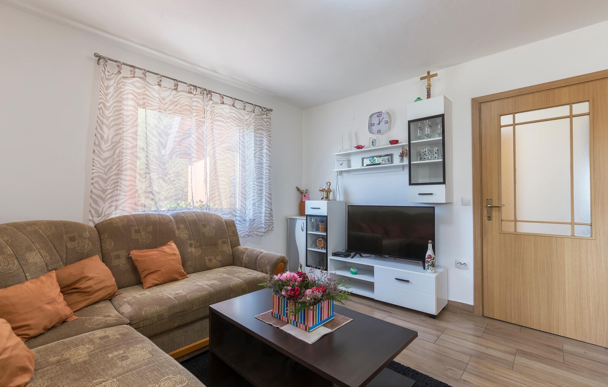 A living room with a sofa, a coffee table with a floral centerpiece, a TV, and a white entertainment unit with shelves.