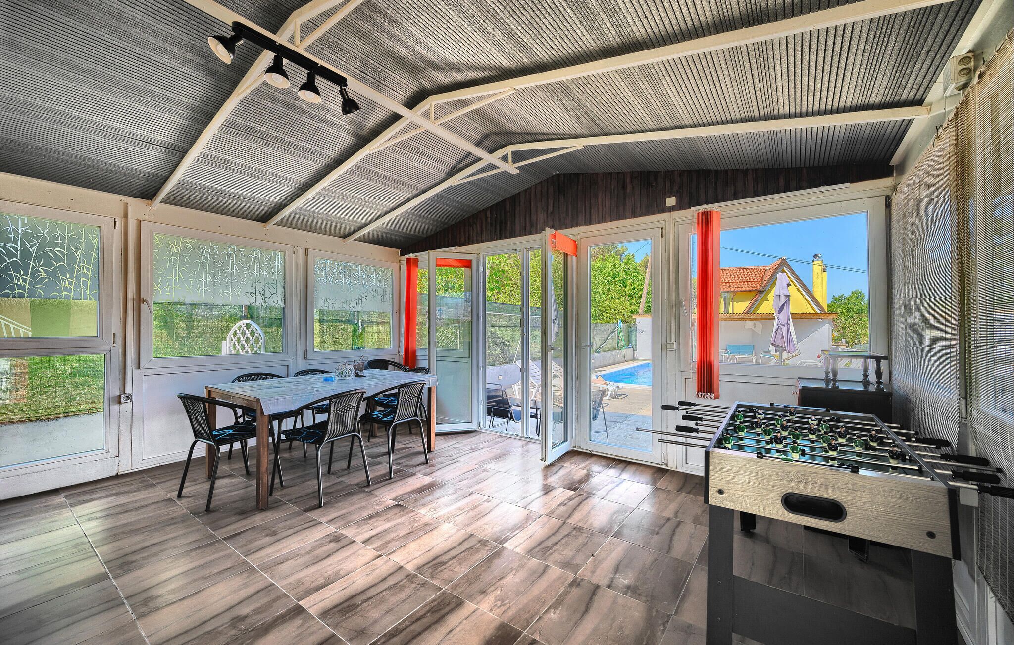 Ein geräumiges Zimmer mit Holztisch und -stühlen, einem Kicker und großen Fenstern mit Blick ins Freie.