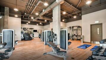 Un gimnasio con máquinas de cardio, equipo de levantamiento de pesas y colchonetas de ejercicio.