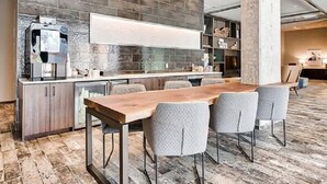 A modern kitchen with a stone backsplash, a coffee machine, and a dining area with a wooden table and grey upholstered chairs. - Bell Overlake (Redmond)