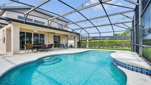 Une piscine entourée de parois en verre, un espace patio avec des chaises et une vue sur un immeuble d’habitation.