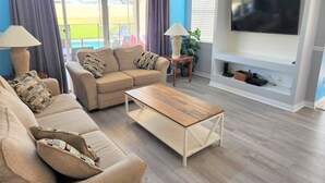 Un salon avec un canapé beige, une table basse en bois et un téléviseur à écran plat fixé au mur.