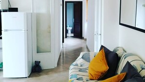 Un salon moderne avec un canapé, un réfrigérateur blanc et un couloir menant à une salle de bain.