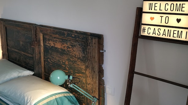 Un lit avec une literie aux tons turquoise et blanc, une lampe de bureau turquoise et un panneau d’accueil accroché au mur.