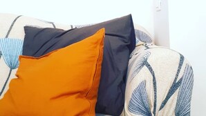 Un salon avec un canapé, plusieurs coussins et une œuvre d’art abstraite encadrée accrochée au mur.