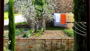Un bâtiment en pierre avec un toit en tuiles, un petit clocher et un jardin agrémenté d’un arbre et d’un fil à linge.
