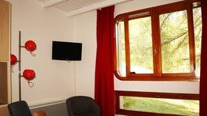 Une pièce dotée d’une grande fenêtre, d’un téléviseur à écran plat, de deux chaises et d’un banc en bois.