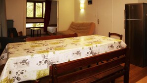 Un coin repas avec une table recouverte d’une nappe à motifs floraux, des chaises en bois, un banc, un canapé et un réfrigérateur.