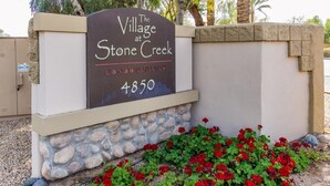 Naamplaatje voor 'Village at Stone Creek Condominiums', met een stenen voet en rode bloemen ervoor.