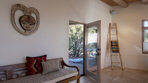 Une pièce avec un banc en bois, un coussin à motifs sur le banc, une échelle en bois et une porte donnant sur l’extérieur.