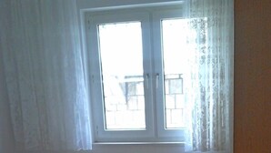 A bedroom with a bed, a window with curtains, a bedside table, and a lamp.