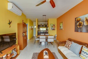 Uma sala de estar com sofá, televisão e um espaço de jantar com cadeiras e mesa.