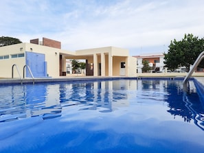 Uma piscina com água azul cristalina, rodeada por edifícios modernos com fachadas bege e castanhas.
