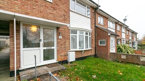 A two-story brick house with a front door, a small garden with grass and fallen leaves, and a satellite dish on the roof. - Denby Lodge (Letchworth)