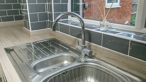 A kitchen with a stainless steel sink, black and white tiles, and a window with a view of a brick building. - Denby Lodge (Letchworth)