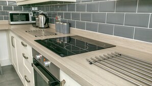 A modern kitchen with a built-in microwave, kettle, and coffee maker, along with a stainless steel range hood and oven. - Denby Lodge (Letchworth)