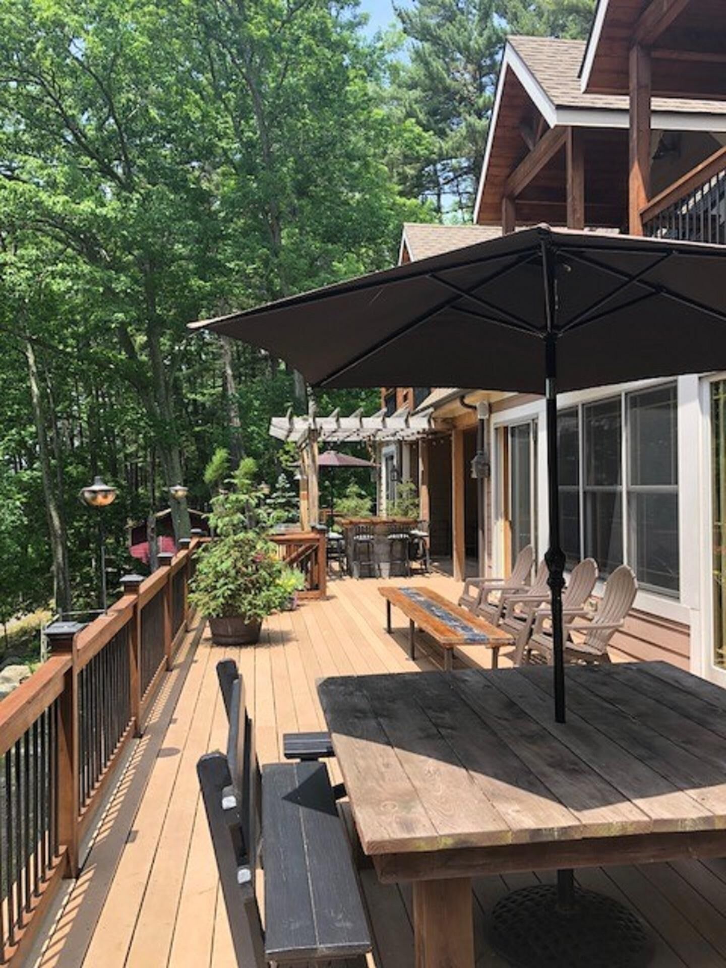 Eine Holzterrasse mit Gartenmöbeln, darunter ein Tisch und Stühle, sowie ein großer Sonnenschirm.