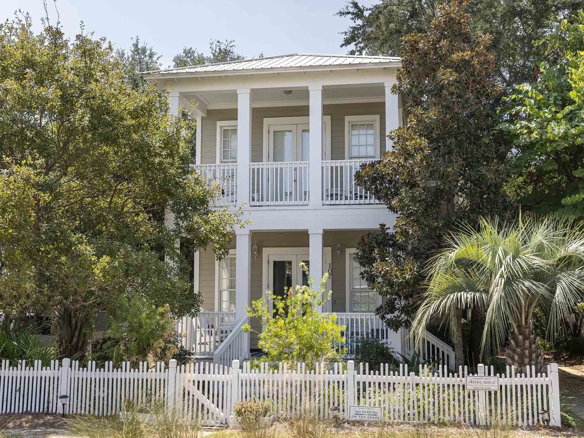 A two-story house with a balcony, surrounded by trees and a white picket fence.