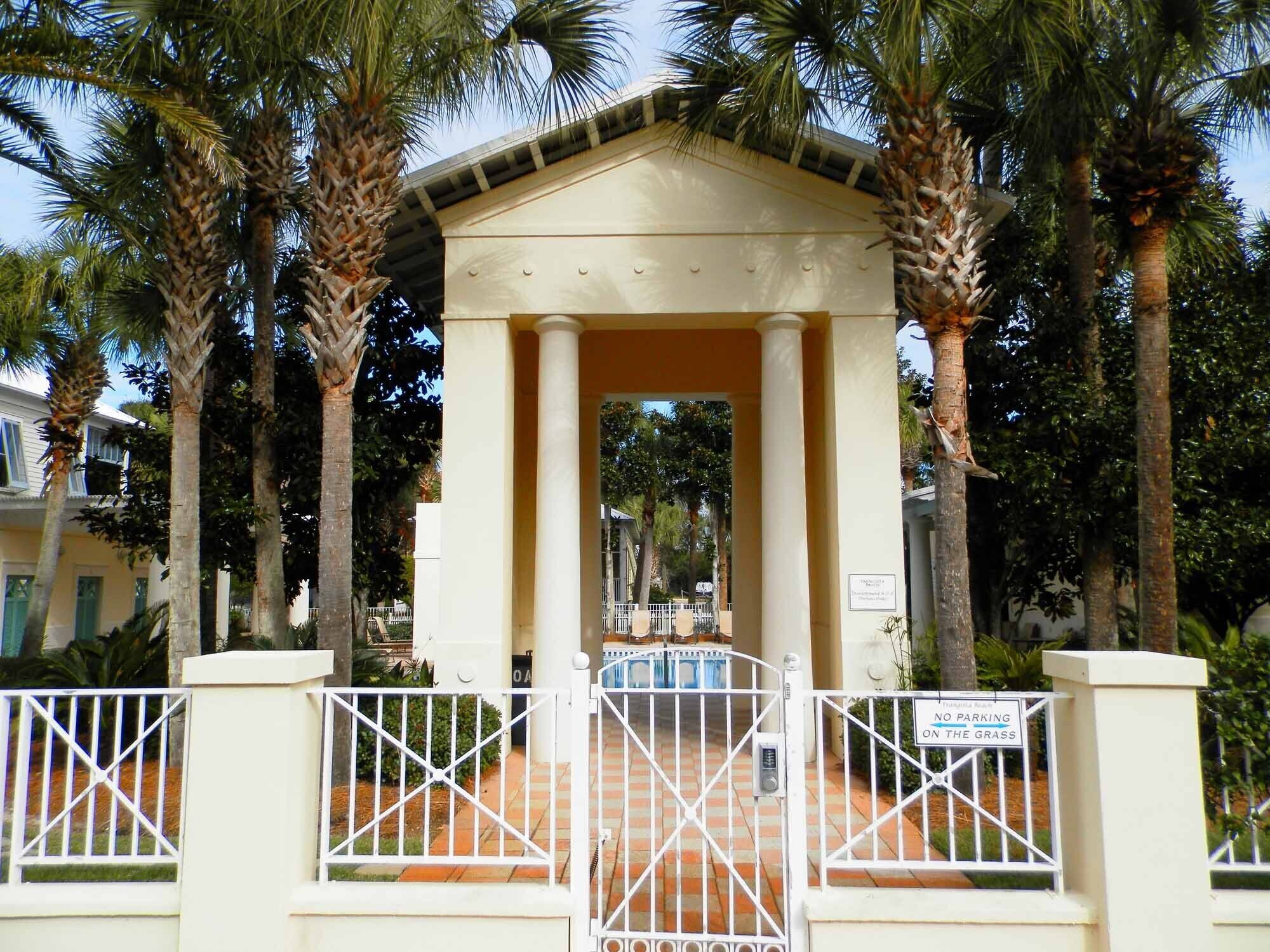 A gated entrance with a covered pavilion, palm trees, and a pool area.