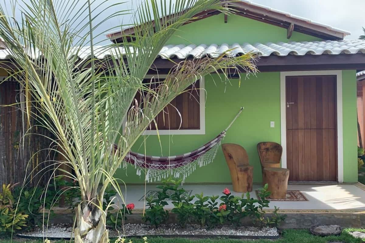 A green house with a tiled roof, a hammock, and two wooden chairs in front.