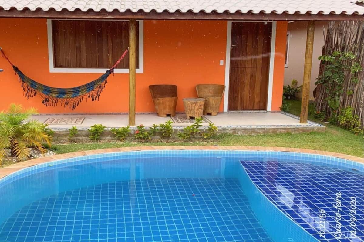 A swimming pool with a tiled edge, a hammock, and a house with an orange facade and a tiled roof.