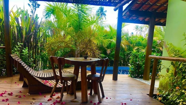 Une terrasse en bois avec une table ronde et des chaises, entourée d’une végétation luxuriante et agrémentée d’un hamac.