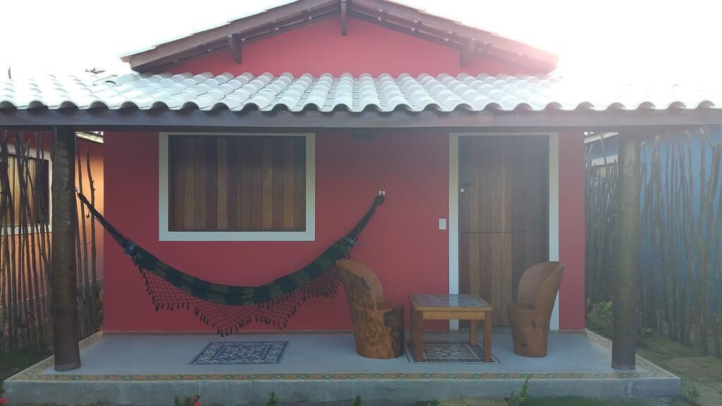 Una casa roja con techo de tejas, una hamaca, una mesa pequeña y una silla en el exterior.