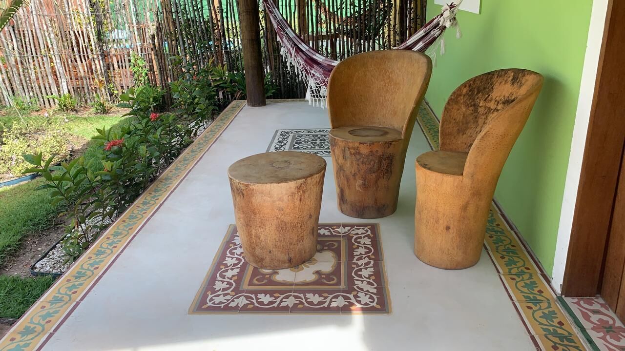 A patio with a hammock, three wooden chairs, and a patterned rug.