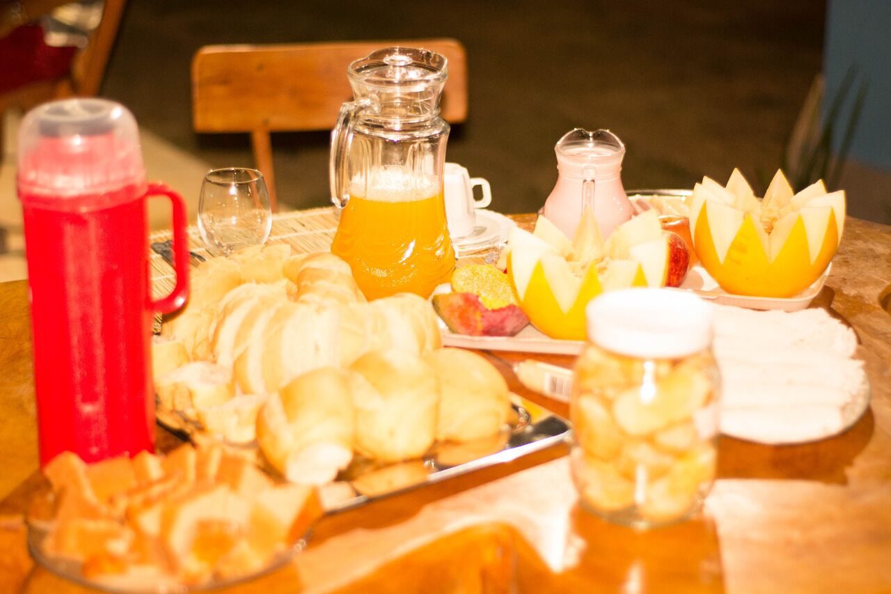 Une table de petit-déjeuner avec un pichet de jus d’orange, un verre d’eau, un pot de lait, des fruits coupés et des viennoiseries.