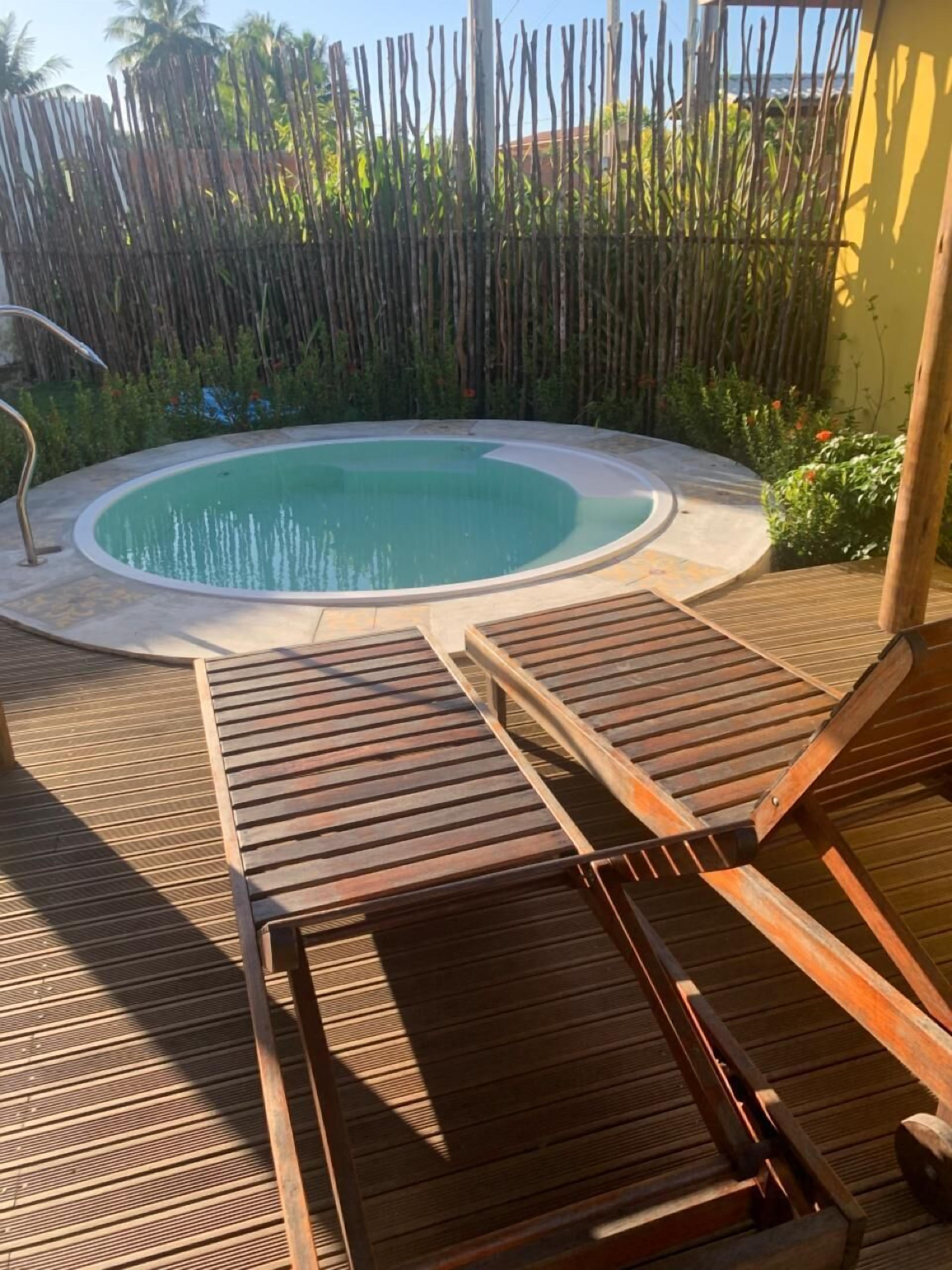 A pool area with two wooden lounge chairs and a small pool.