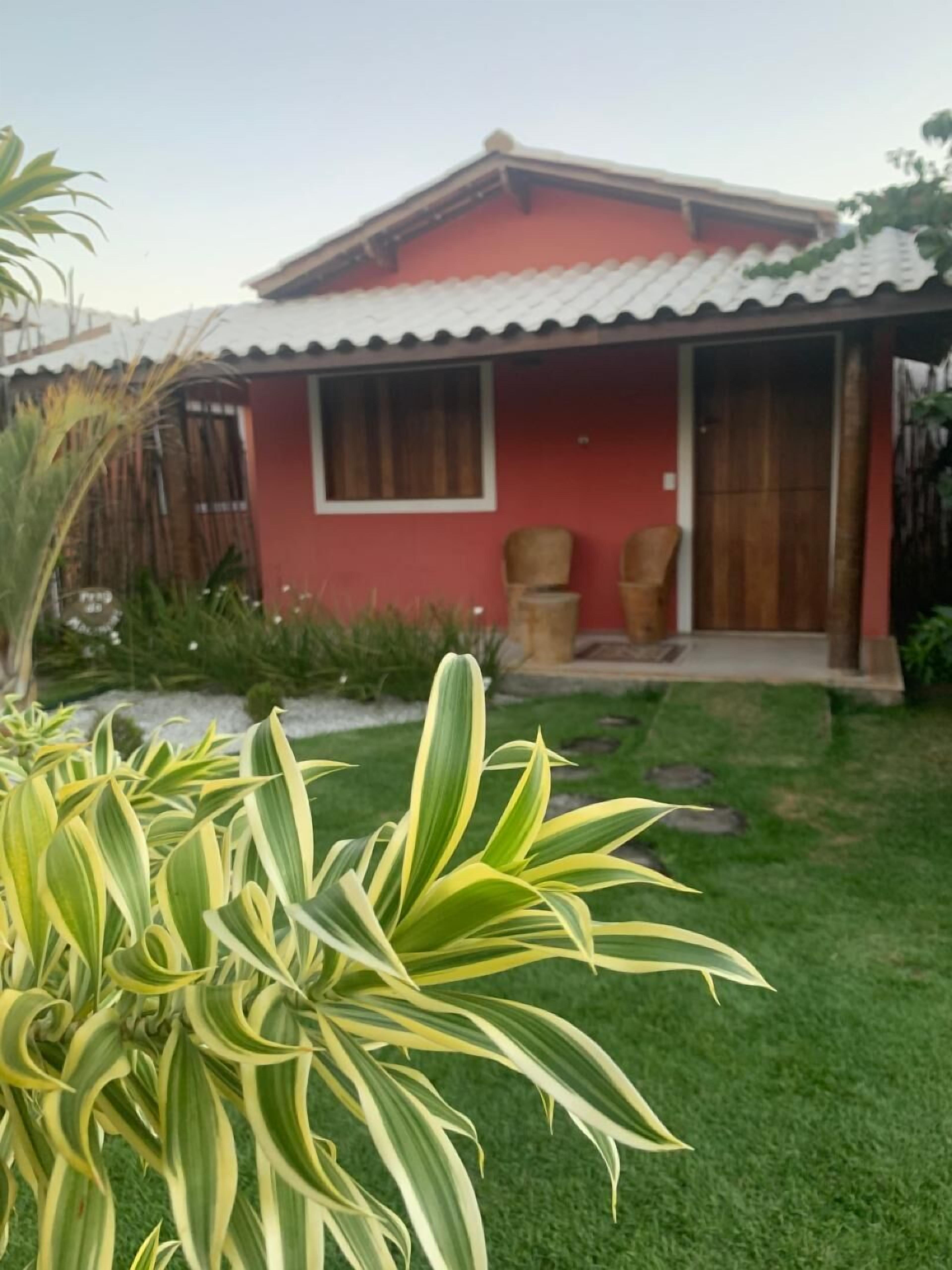 Una casa roja con techo de tejas, un porche con dos sillas y un césped bien cuidado.