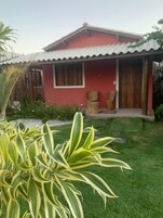 Una casa roja con techo de tejas, un porche con dos sillas y un césped bien cuidado.