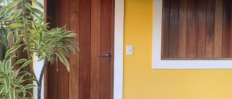 Un edificio con una puerta de madera y una ventana. Hay plantas al frente.
