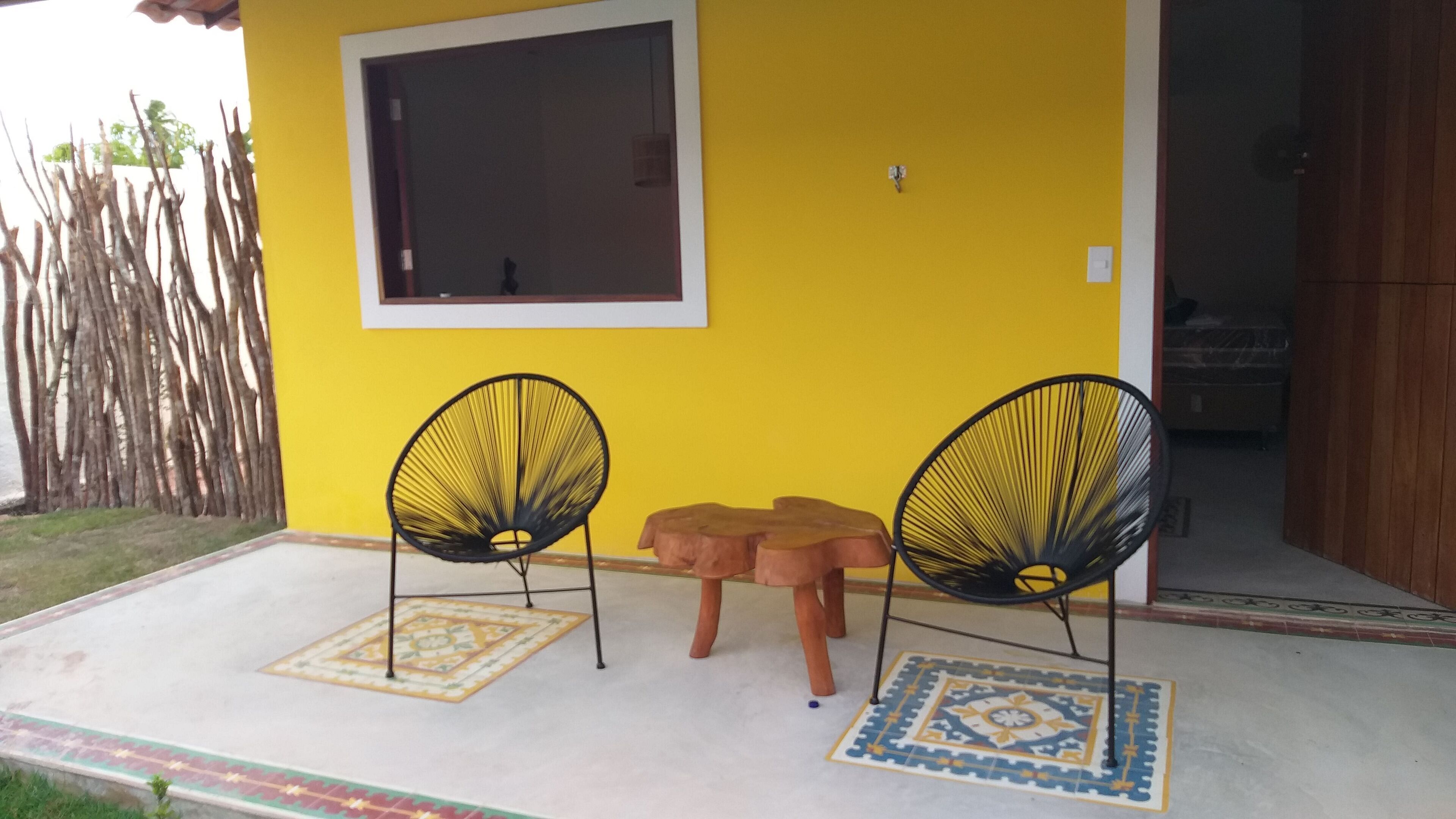 A yellow wall with a window and two black chairs with woven seats.