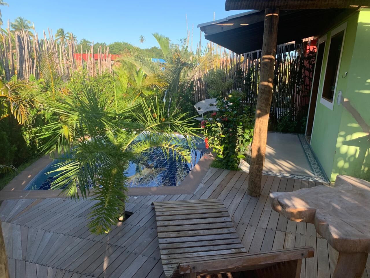 A wooden deck with a pool, surrounded by tropical plants and a bamboo fence.