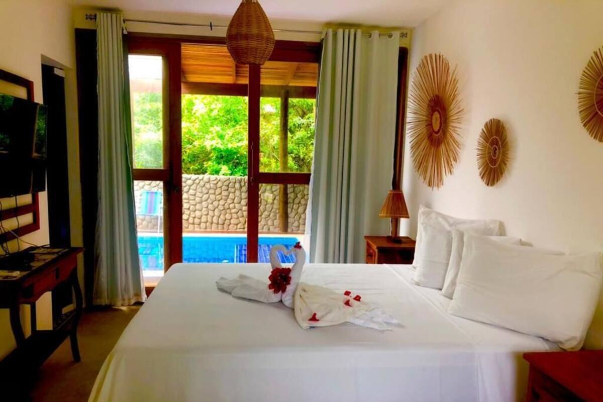 A hotel room with a bed, a TV, a desk, and a view of a swimming pool.