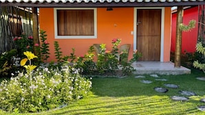 Une maison avec un toit en tuiles, une porte en bois et un petit porche. Un jardin avec différentes plantes et fleurs se trouve devant la maison.