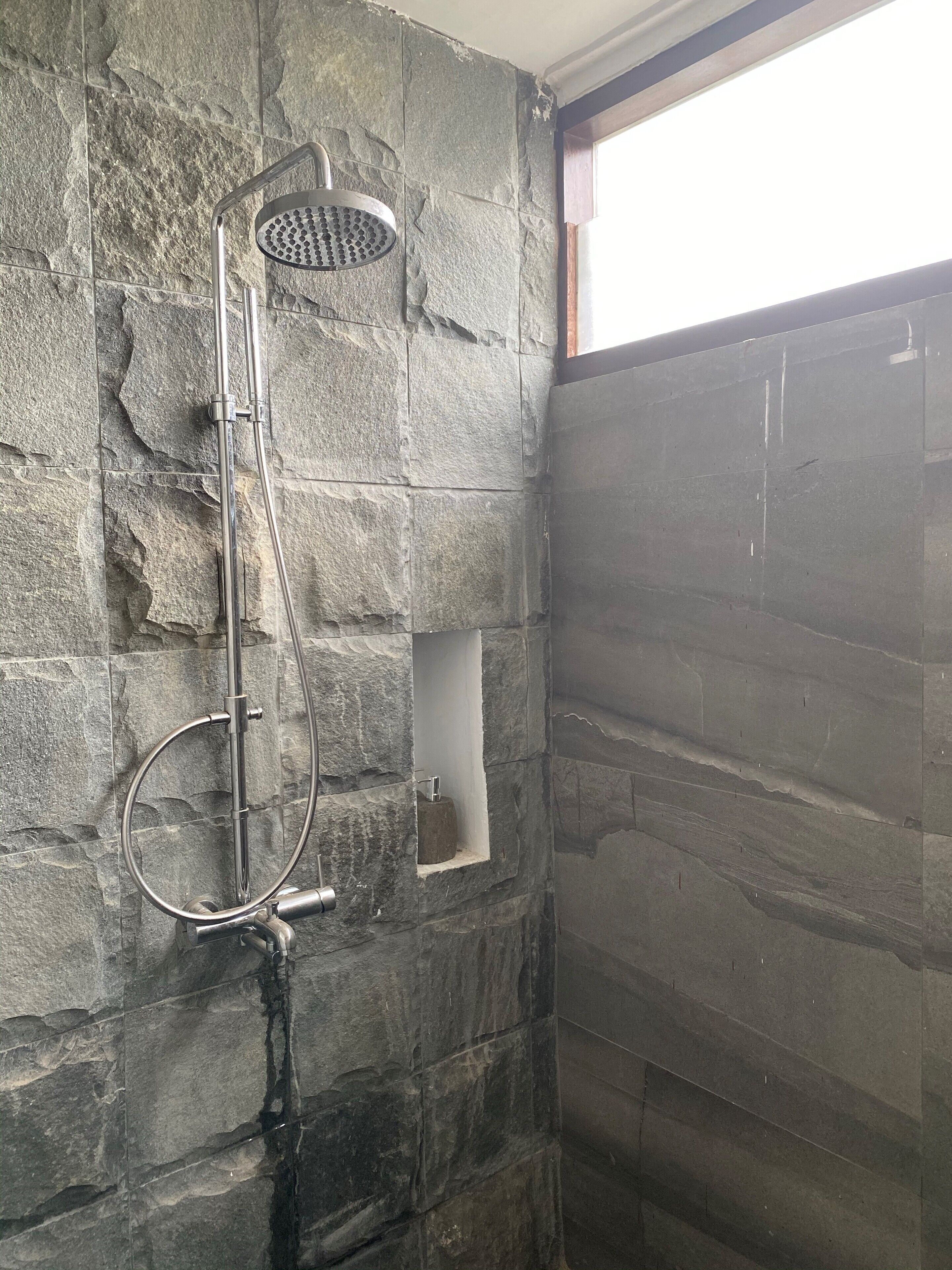 Une douche équipée d’un pommeau de douche à main et d’un pommeau de douche à pluie fixé au mur, le tout installé devant un mur en pierre à texture.