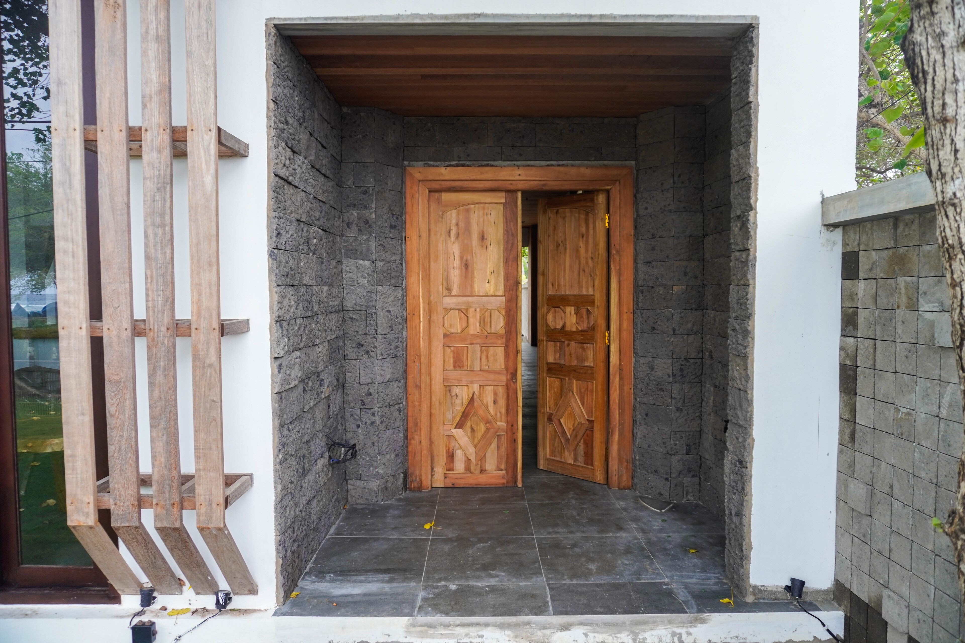 A wooden door with a geometric pattern, set in a stone wall entrance with a tiled floor.