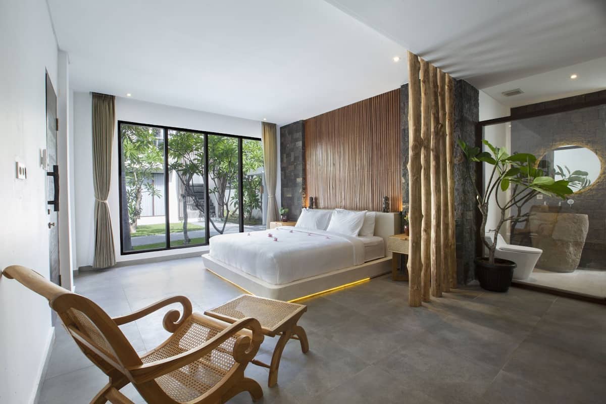A modern bedroom with a large bed, a wooden chair, a potted plant, and a stone wall.