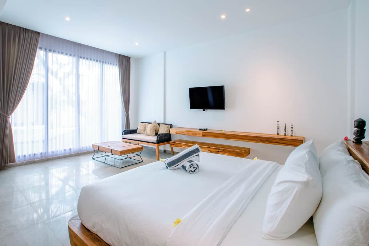 A modern hotel room with a large bed, a sofa, a TV mounted on the wall, and a wooden bench.