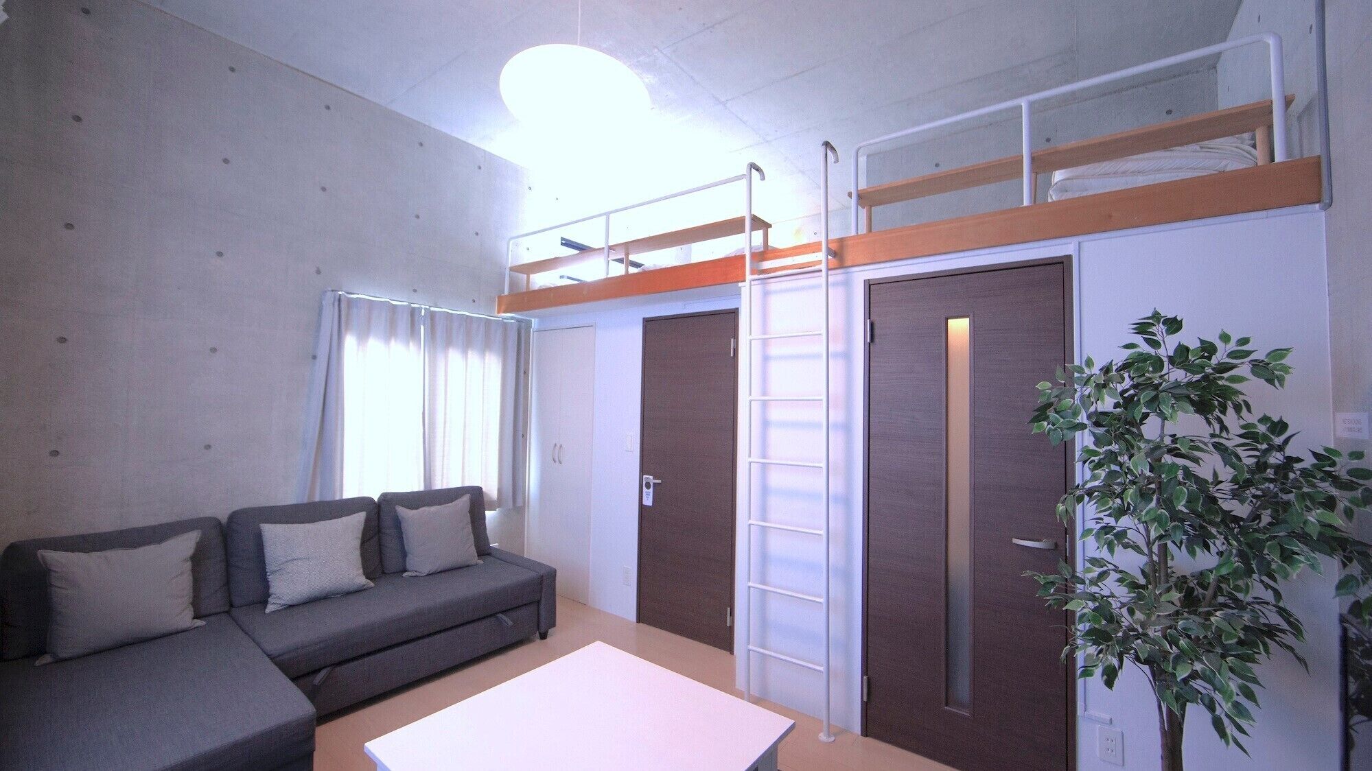 A compact living space with a sofa, a small table, a bunk bed, and a door.