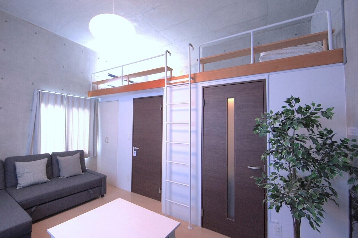 A compact living space with a sofa, a small table, a bunk bed, and a door.