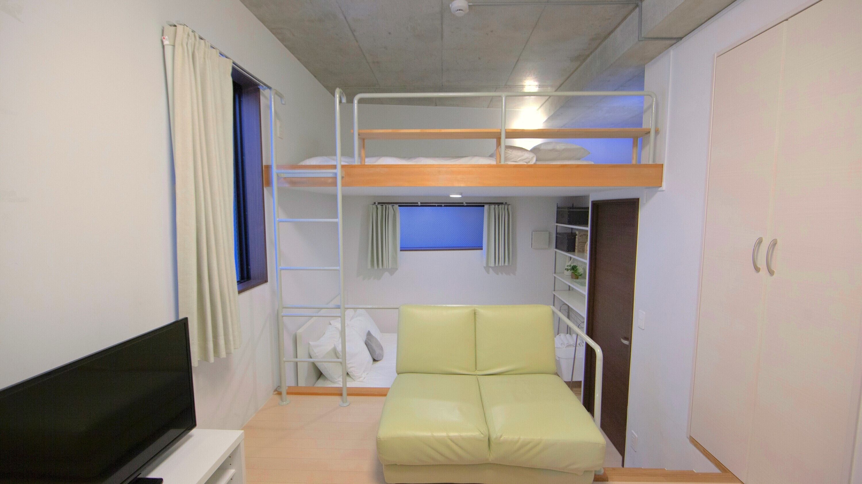A bunk bed room with a TV, a green sofa, and a window with curtains.