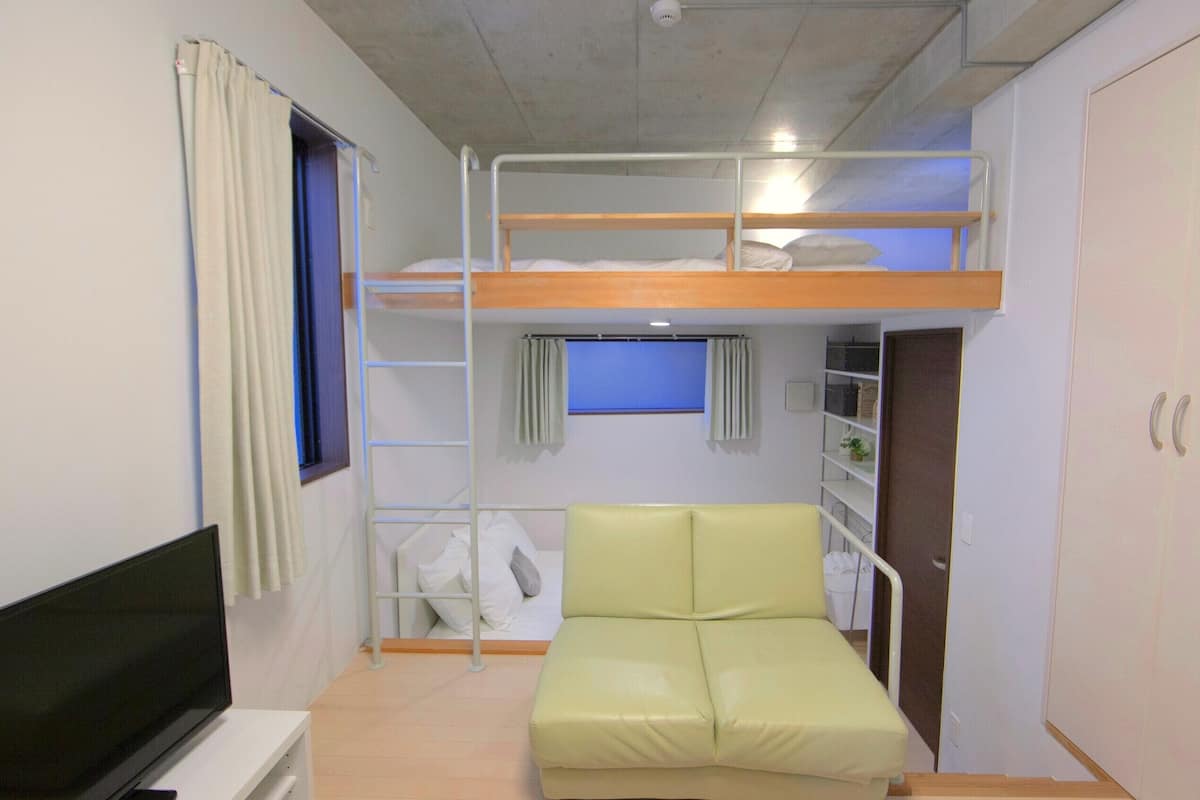 A bunk bed room with a TV, a green sofa, and a window with curtains.