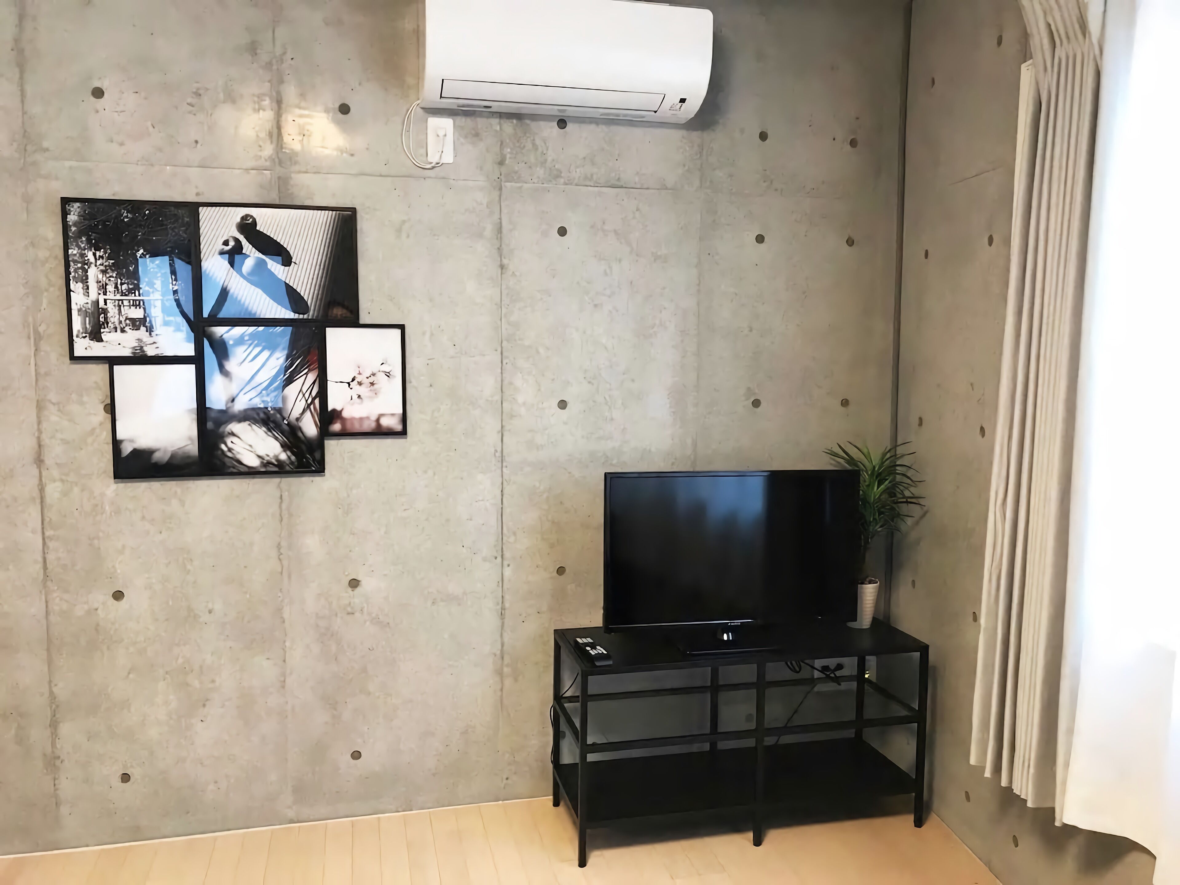 Una sala de estar con un televisor de pantalla plana sobre un soporte negro, una planta en maceta y un aire acondicionado instalado en la pared.