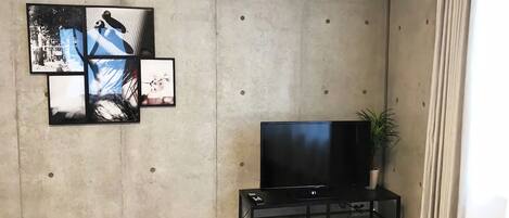 Una sala de estar con un televisor de pantalla plana sobre un soporte negro, una planta en maceta y un aire acondicionado instalado en la pared.