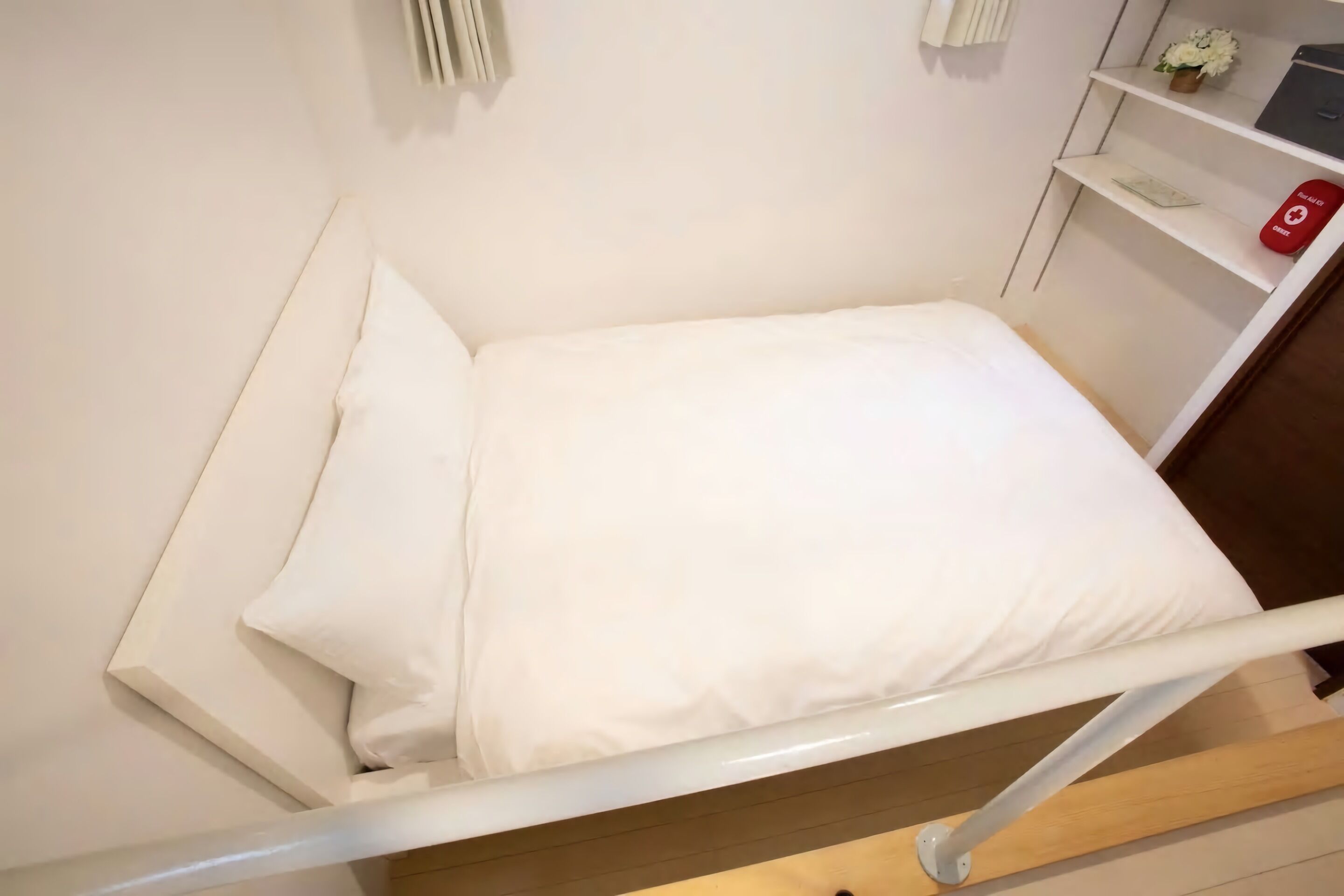 A neatly made bed with white linens in a room with a wooden floor and white walls.