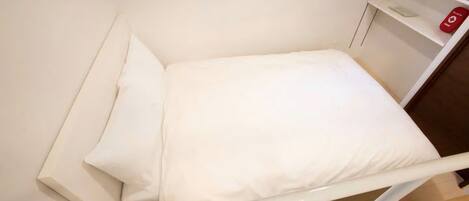 A neatly made bed with white linens in a room with a wooden floor and white walls.