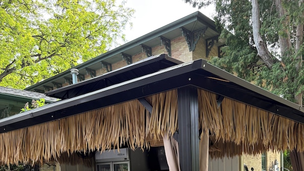 Zona de bar al aire libre con techo de paja, taburetes y un vehículo estacionado cerca.